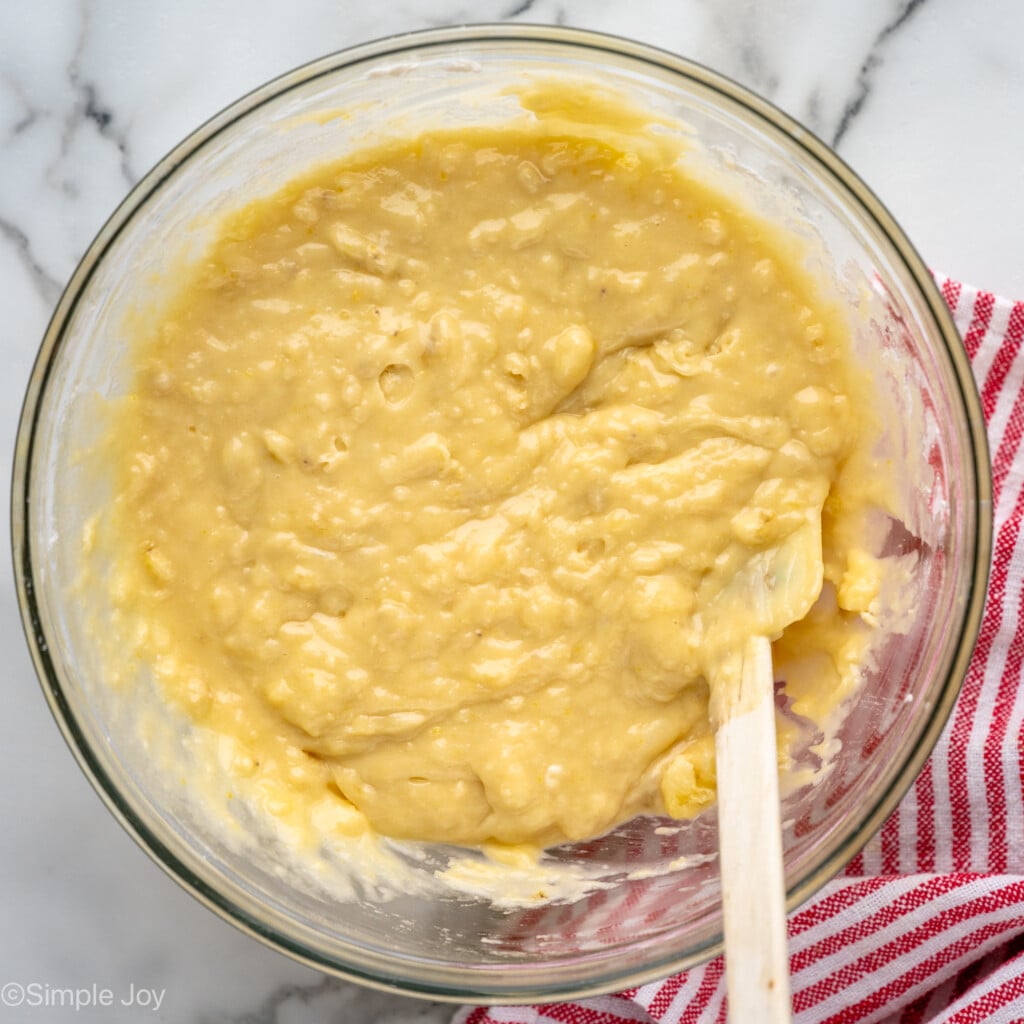 Overhead view of ingredients for banana chocolate chip muffins in a mixing bowl with a spatula for stirring.