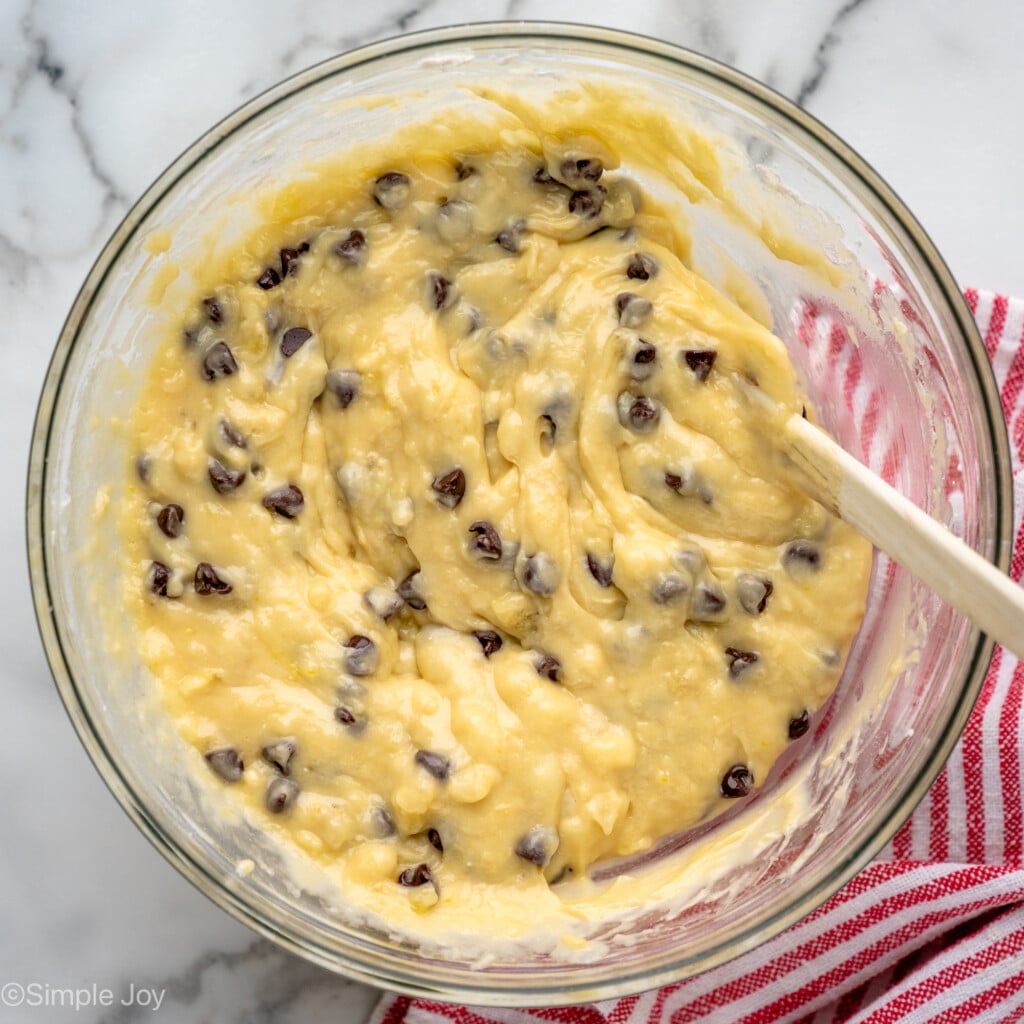 Overhead view of a mixing bowl of batter for banana chocolate chip muffins recipe with a spatula for stirring.