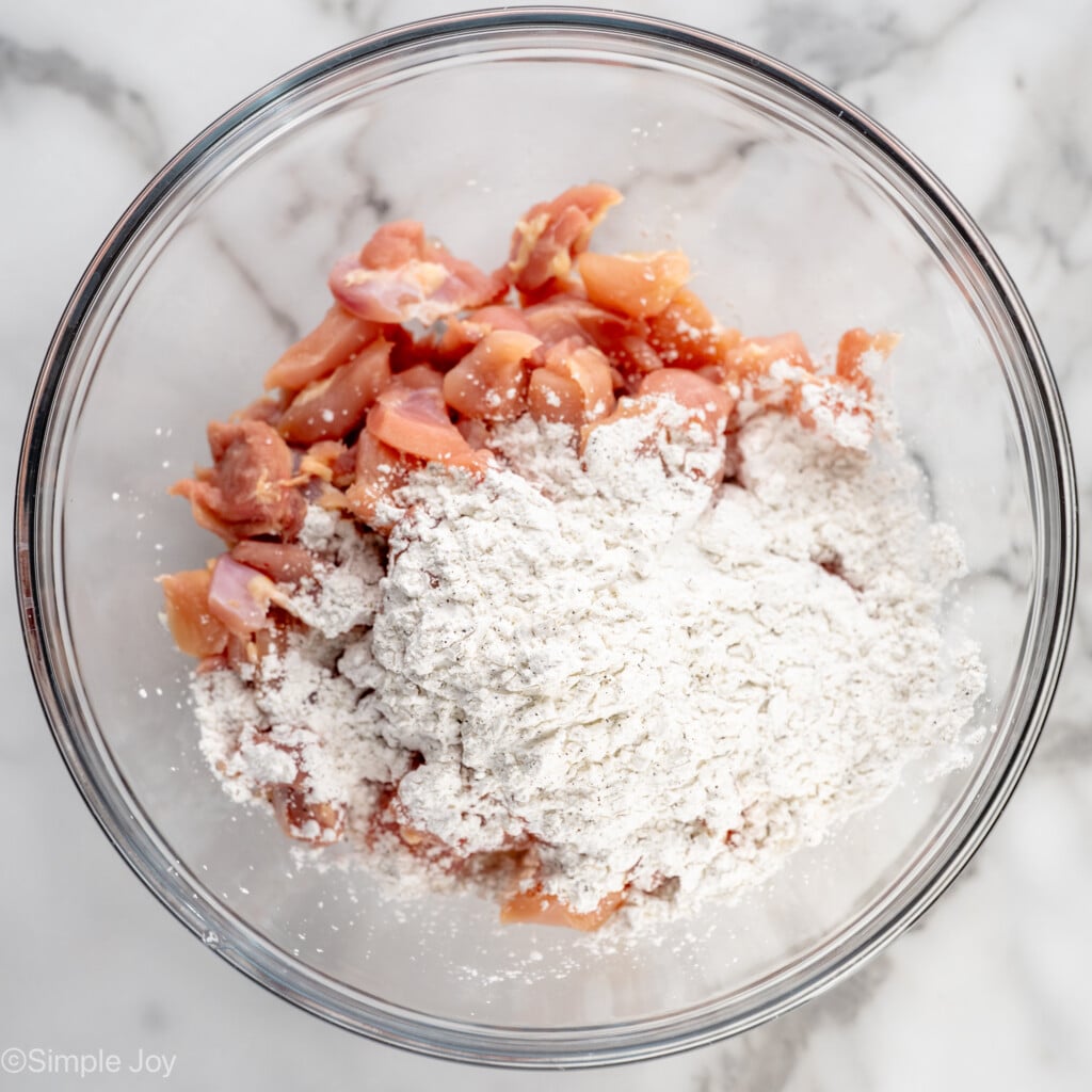 Overhead view of mixing bowl of raw chicken pieces and flour mixture for Bourbon Chicken recipe - 7