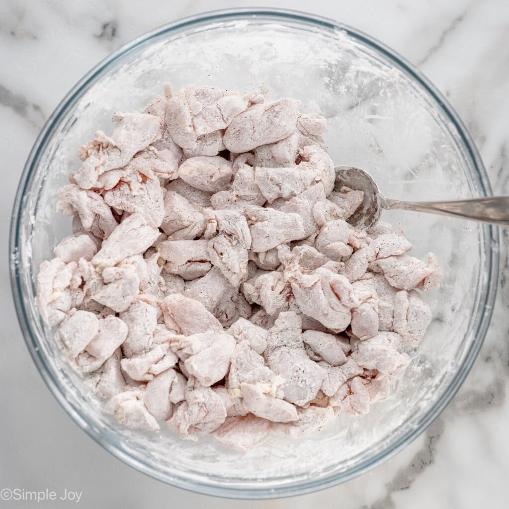 Overhead view of a mixing bowl of pieces of chicken in breading with spoon for Bourbon Chicken recipe