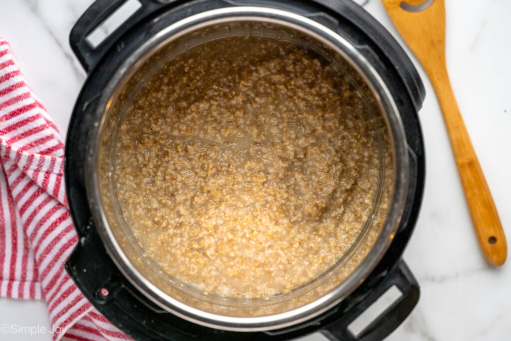 Overhead view of an instant pot with ingredients for Instant Pot Steel Cut Oats recipe, wooden spoon beside. - 9
