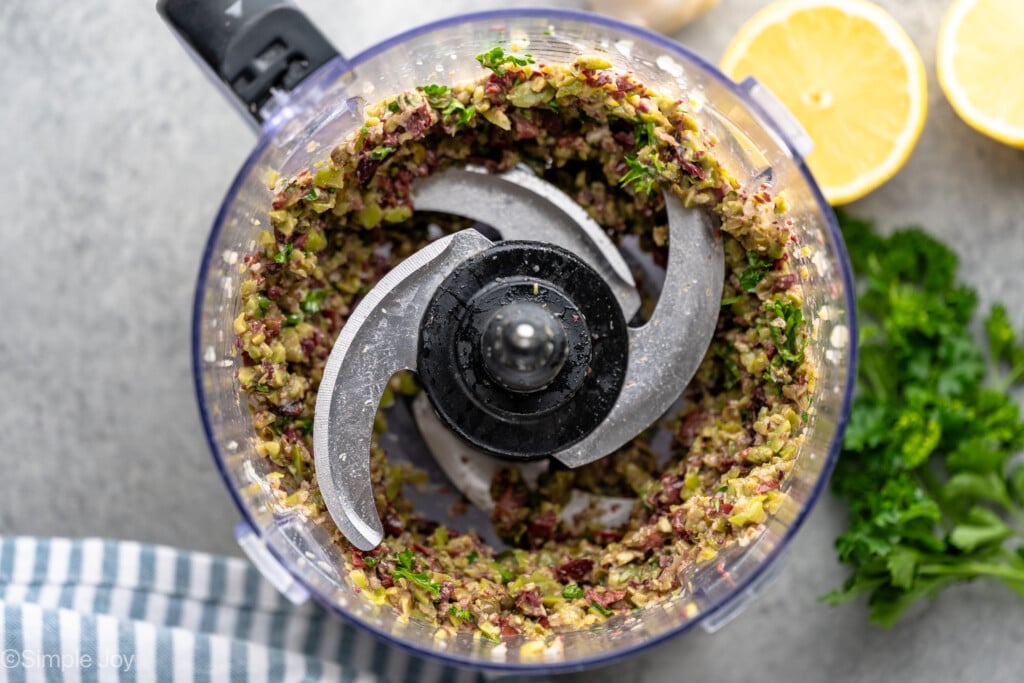 Overhead view of food processor with Olive Tapenade recipe, lemons and parsley beside. - 7