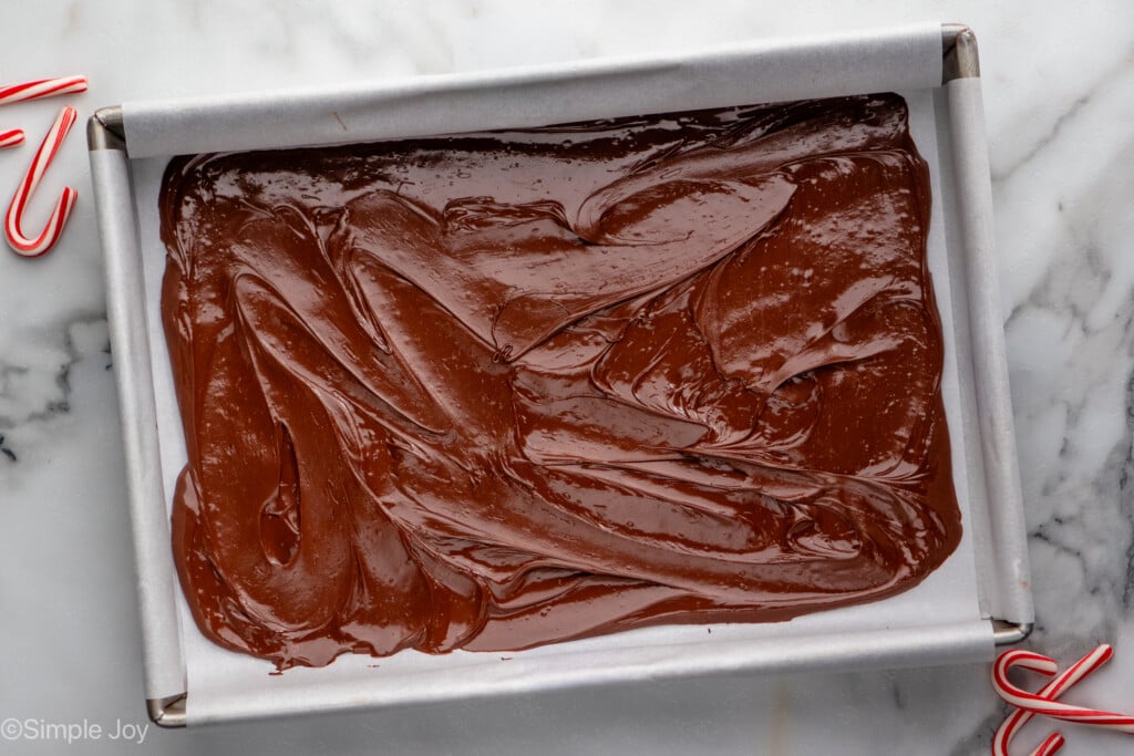 Overhead view of a sheet pan with the bottom layer of Peppermint Bark recipe, candy canes beside. - 8