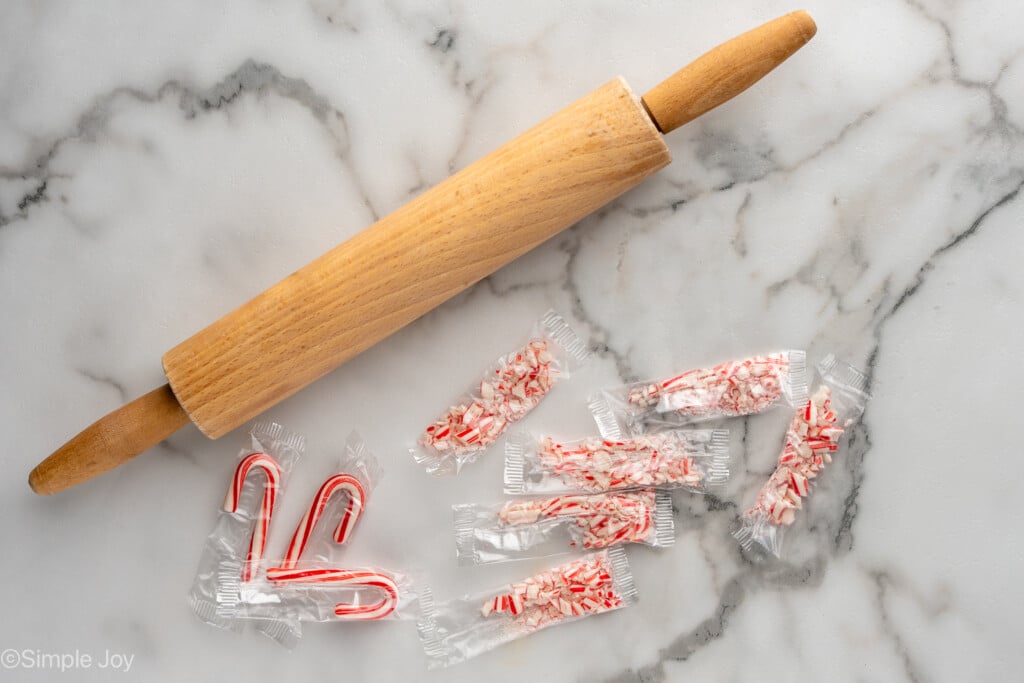 Overhead view of a rolling pin and mini candy canes, some crushed, for Peppermint Bark recipe - 7