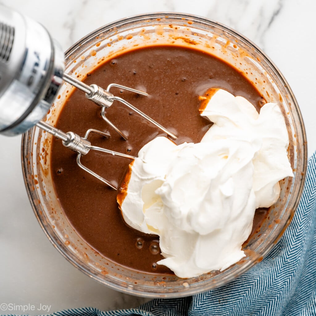 Overhead view of mixing bowl of pudding mix with whipped cream, hand mixer for Pudding Shots recipe. - 7