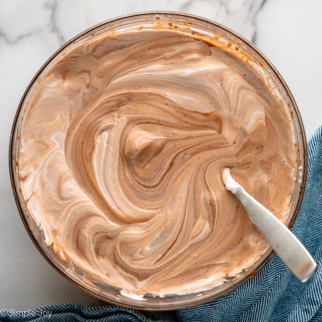 Overhead view of a mixing bowl of ingredients with spoon stirring for Pudding Shots recipe.