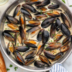 Overhead view of a skillet of Mussels recipe, bread and white wine beside - 11