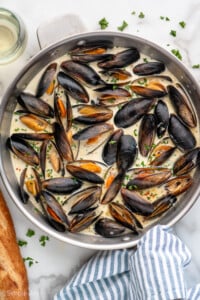 Overhead view of a skillet of Mussels recipe, bread and white wine beside - 10