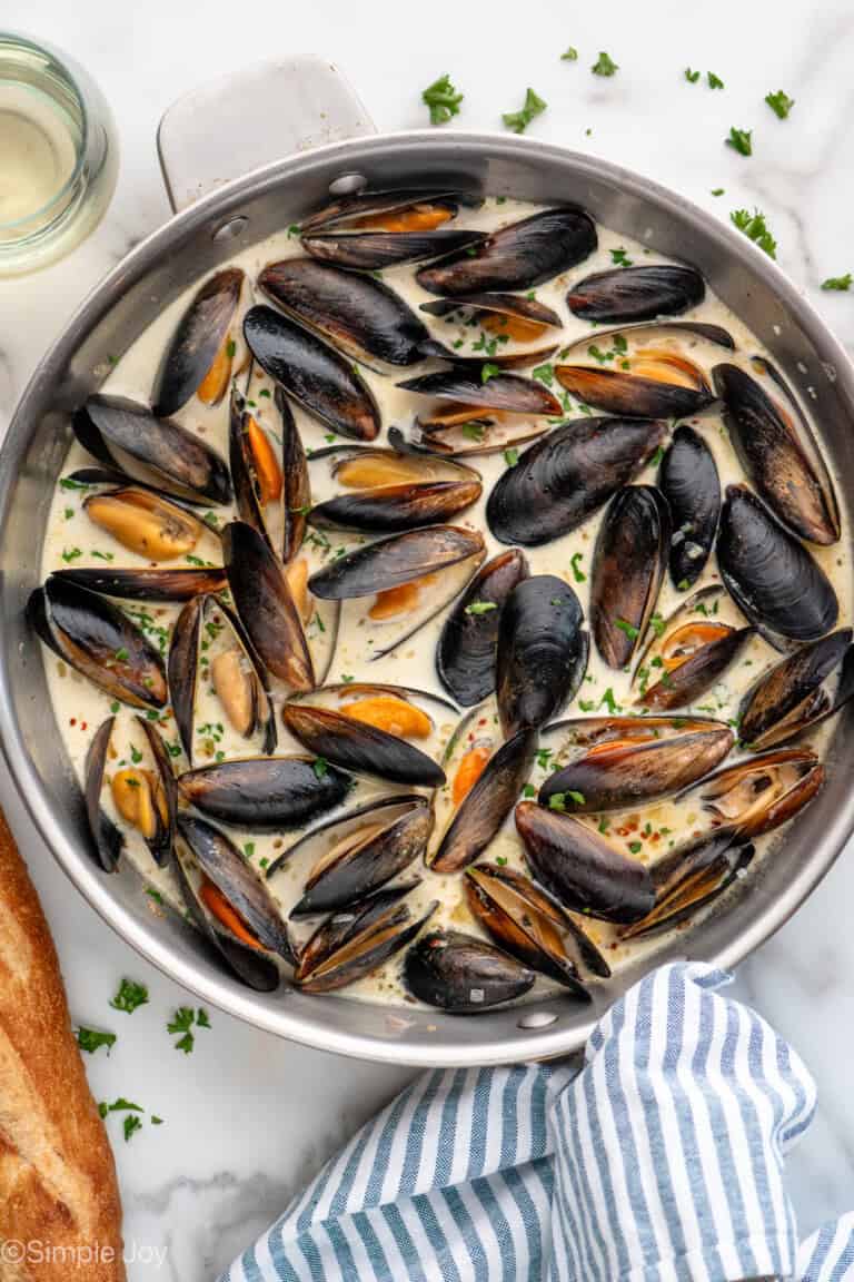 Overhead view of a skillet of Mussels recipe, bread and white wine beside