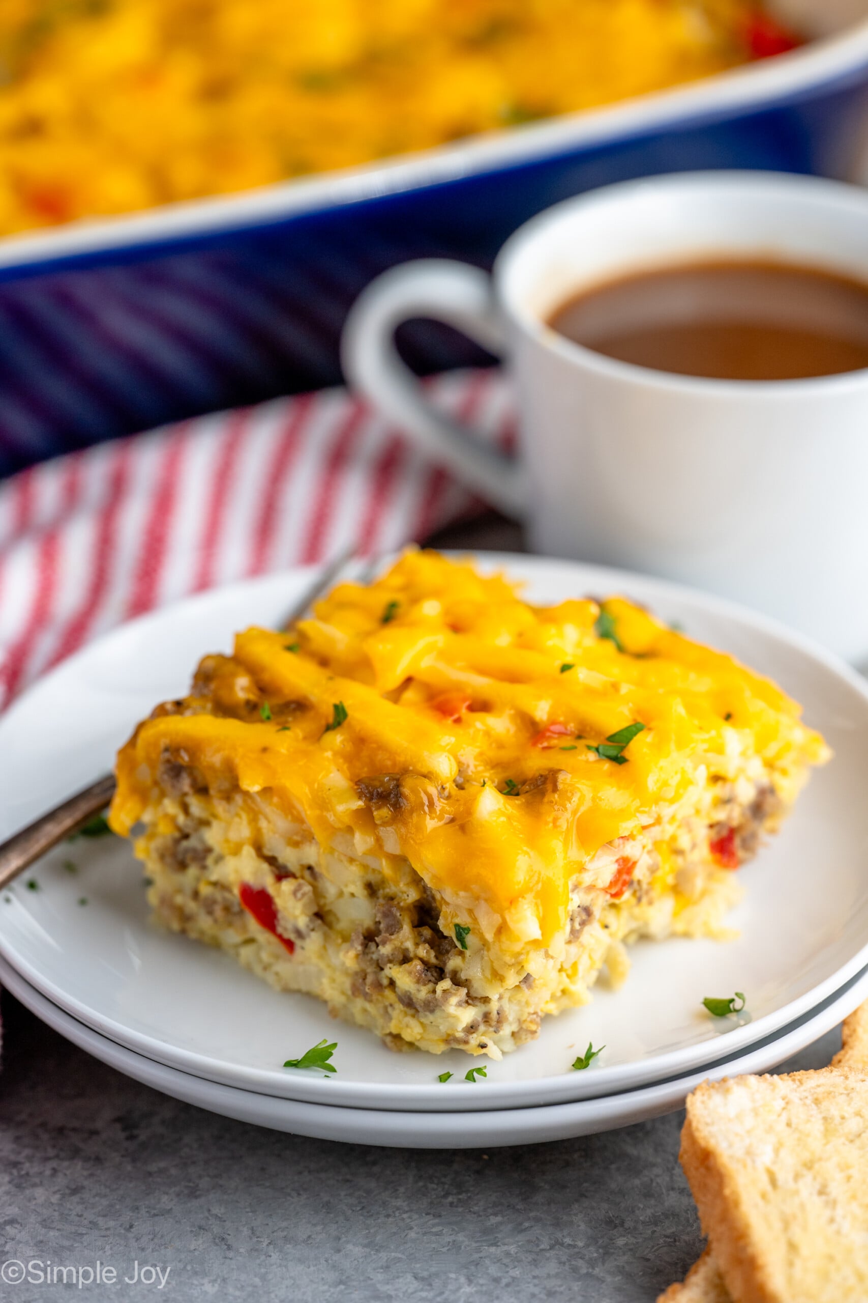Piece of Hashbrown Breakfast Casserole served on a plate with a fork, cup of coffee beside. - 18