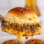 Pinterest graphic for Cheeseburger Sliders recipe. Text says, "the best Cheeseburger Sliders simplejoy.com." Image shows Cheeseburger Slider being lifted from baking dish of Cheeseburger Sliders, garnished with sesame seeds.