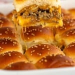 Pinterest graphic for Cheeseburger Sliders recipe. Images a Cheeseburger Slider being lifted from baking dish of Cheeseburger Sliders garnished with sesame seeds. Text says, "super easy Cheeseburger Sliders simplejoy.com."