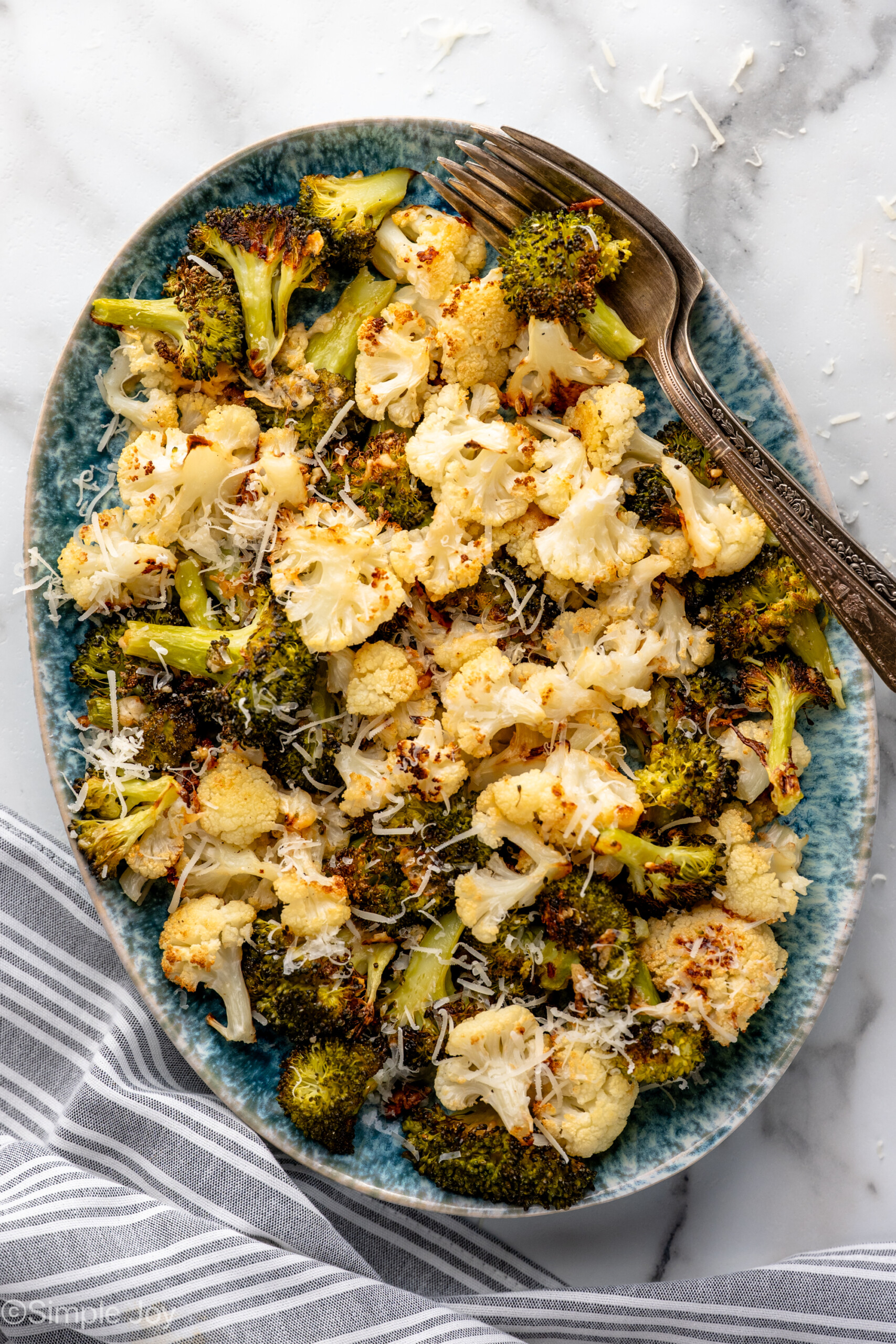 Overhead view of a platter of Roasted Broccoli and Cauliflower garnished with parmesan cheese, forks beside
