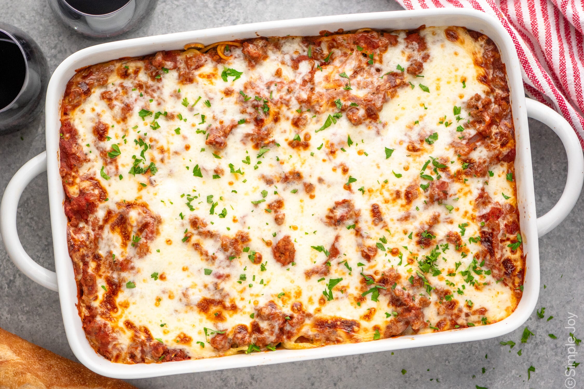 Overhead view of a baking dish of Baked Spaghetti with glasses of red wine beside. - 12