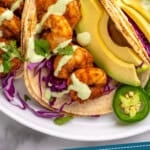 Pinterest graphic for Easy Shrimp Tacos recipe. Image shows Easy Shrimp Tacos garnished with avocado slices, dressing, jalapenos, and cabbage. Text says, "tried & tested Shrimp Tacos simplejoy.com"