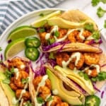 Pinterest graphic for Shrimp Tacos recipe. Text says, "the best Shrimp Tacos recipe simplejoy.com." Image shows overhead view of plate of Shrimp Tacos garnished with dressing, avocado, jalapenos, and cabbage.
