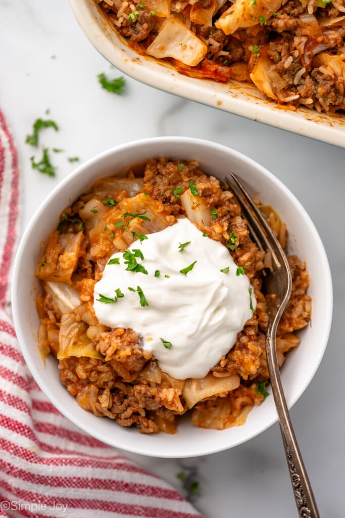Overhead view of a bowl of cabbage roll casserole topped with sour cream and chopped parsley. Fork in bowl.