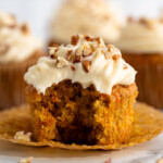 Side view of Carrot Cake Cupcake topped with cream cheese frosting and chopped walnuts, with bite taken out.