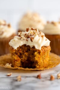 Side view of Carrot Cake Cupcake topped with cream cheese frosting and chopped walnuts, with bite taken out.