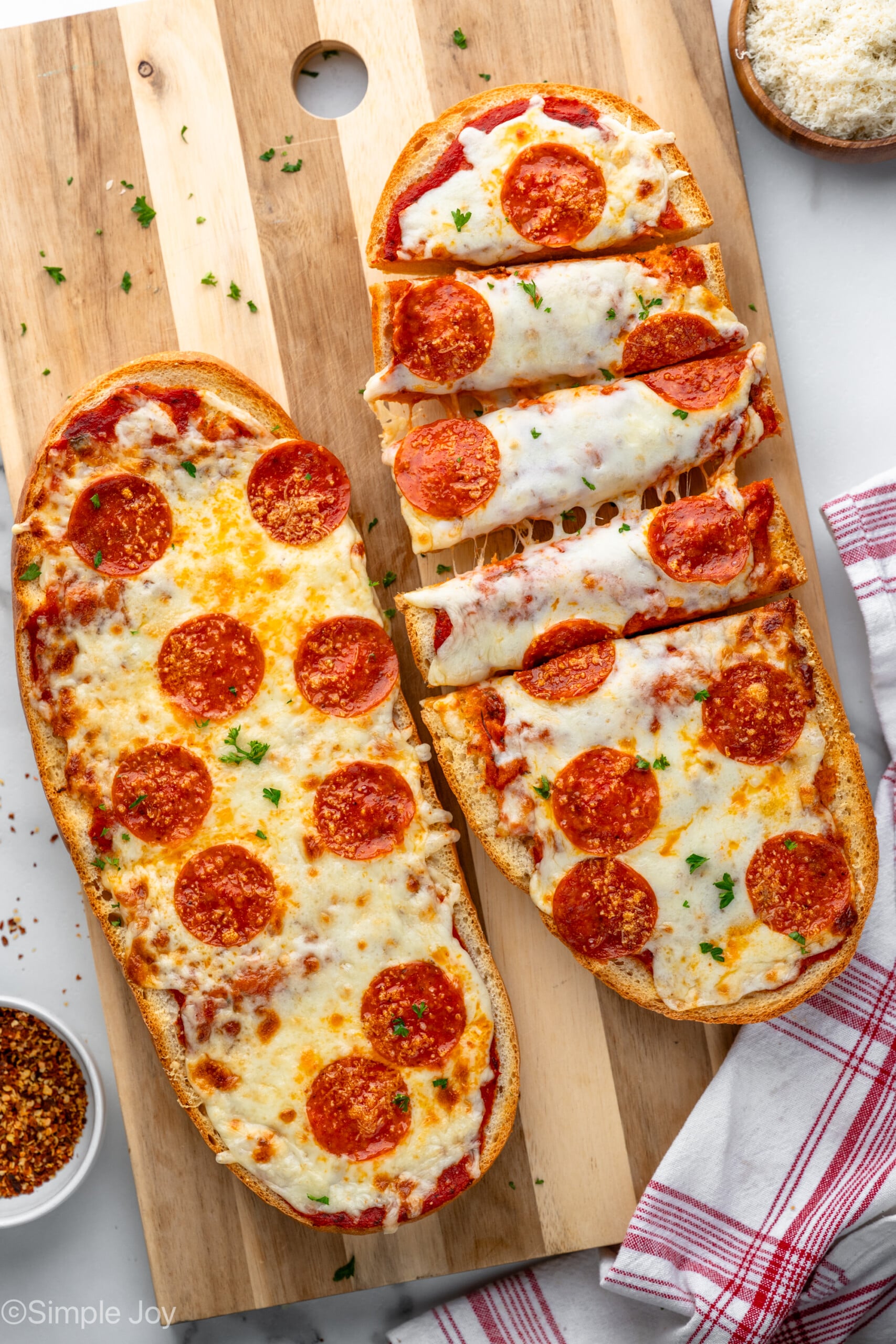 Overhead view of French Bread Pizza served on wooden board with one French Bread Pizza cut into strips