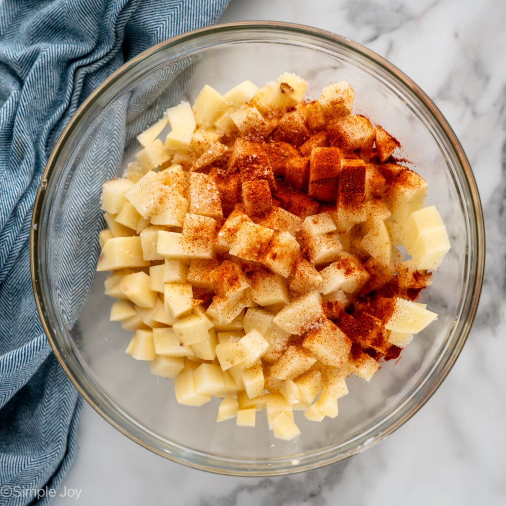 Overhead view of mixing bowl of diced potatoes with seasonings for Air Fryer Breakfast Potatoes recipe