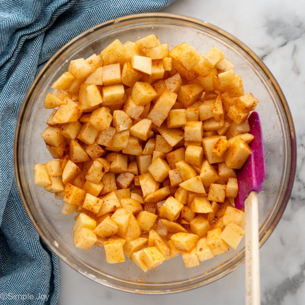 Overhead view of mixing bowl of diced potatoes and seasonings with spatula for Air Fryer Breakfast Potatoes recipe