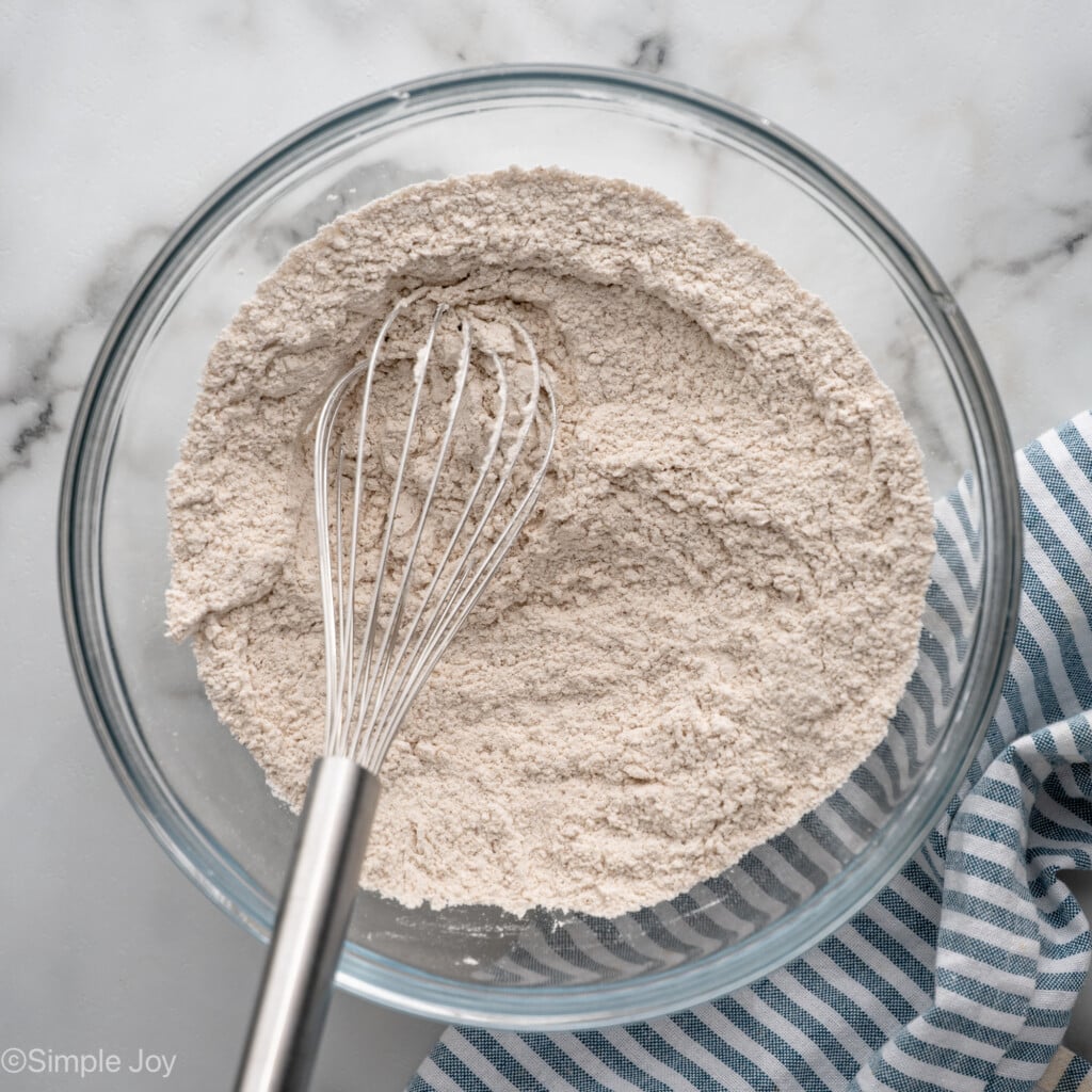 Overhead view of a mixing bowl of dry ingredients for Carrot Cake Cupcakes recipe with a whisk for stirring.