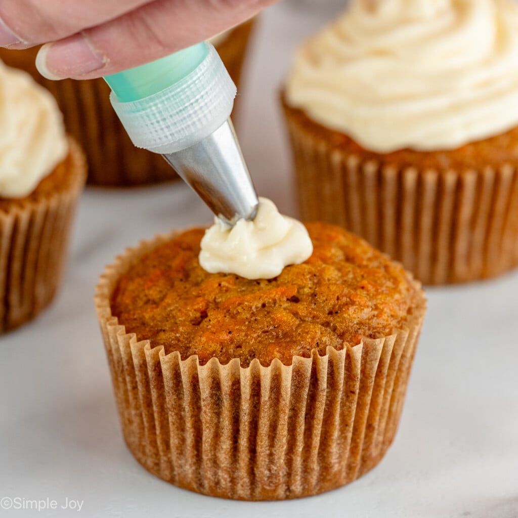 Photo of person's hand frosting Carrot Cake Cupcakes with cream cheese frosting