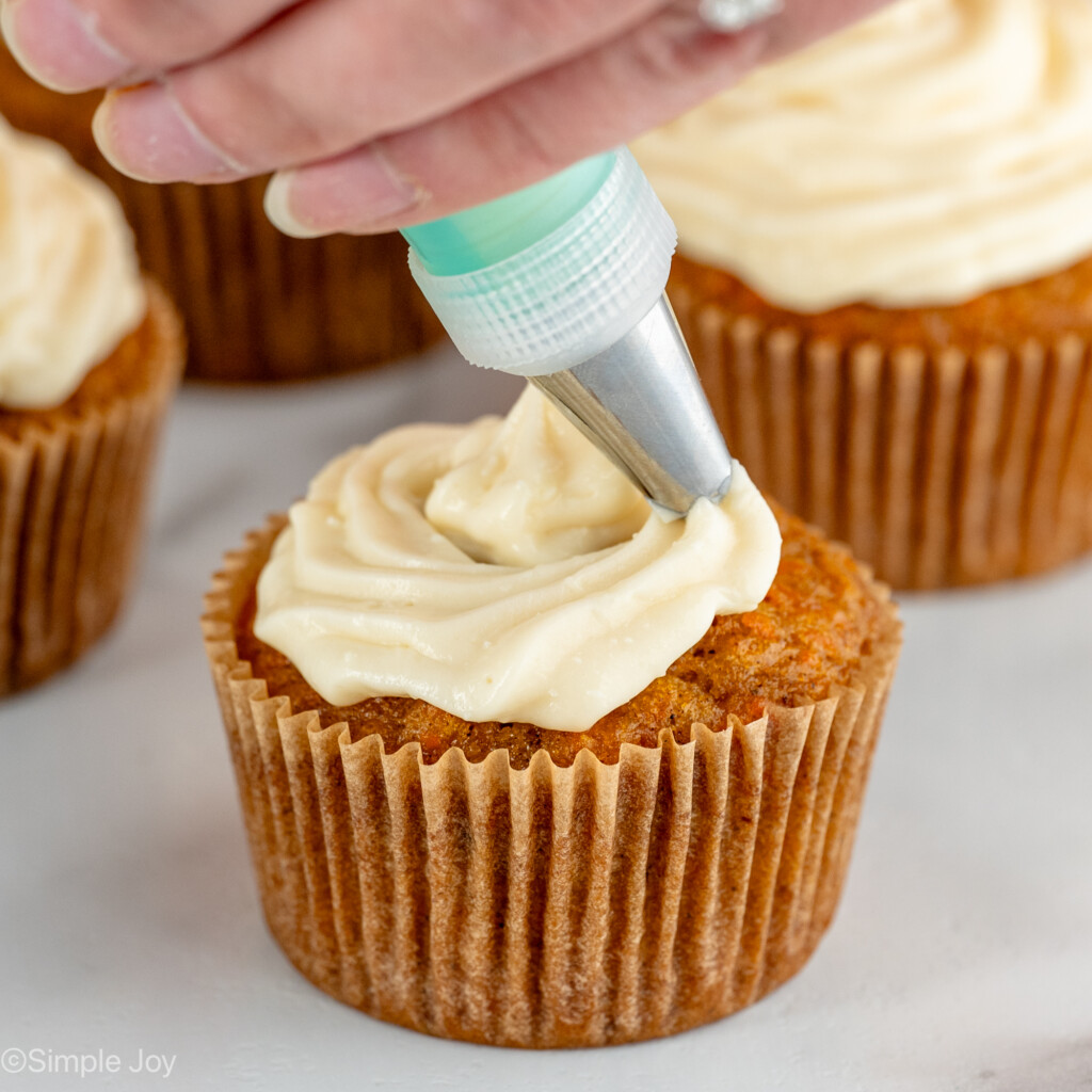 Photo of person's hand frosting Carrot Cake Cupcakes with cream cheese frosting