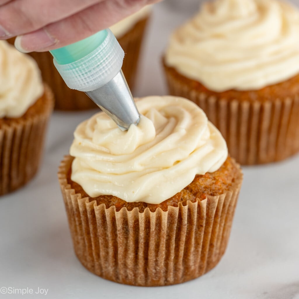 Photo of person's hand frosting Carrot Cake Cupcakes with cream cheese frosting