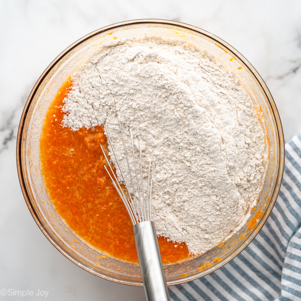 Overhead view of a mixing bowl of ingredients for Carrot Cake Cupcakes recipe with a whisk