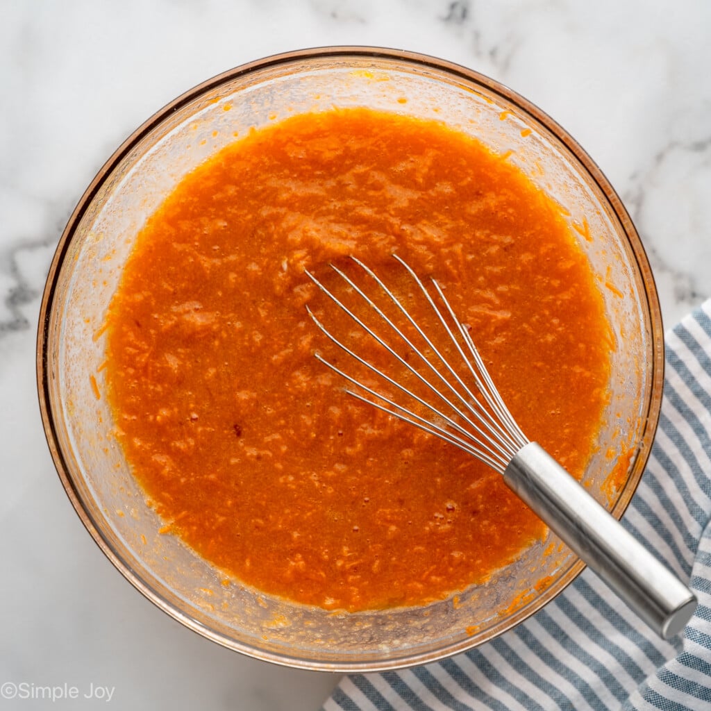Overhead view of combined wet ingredients in a mixing bowl with a whisk for Carrot Cake Cupcakes recipe