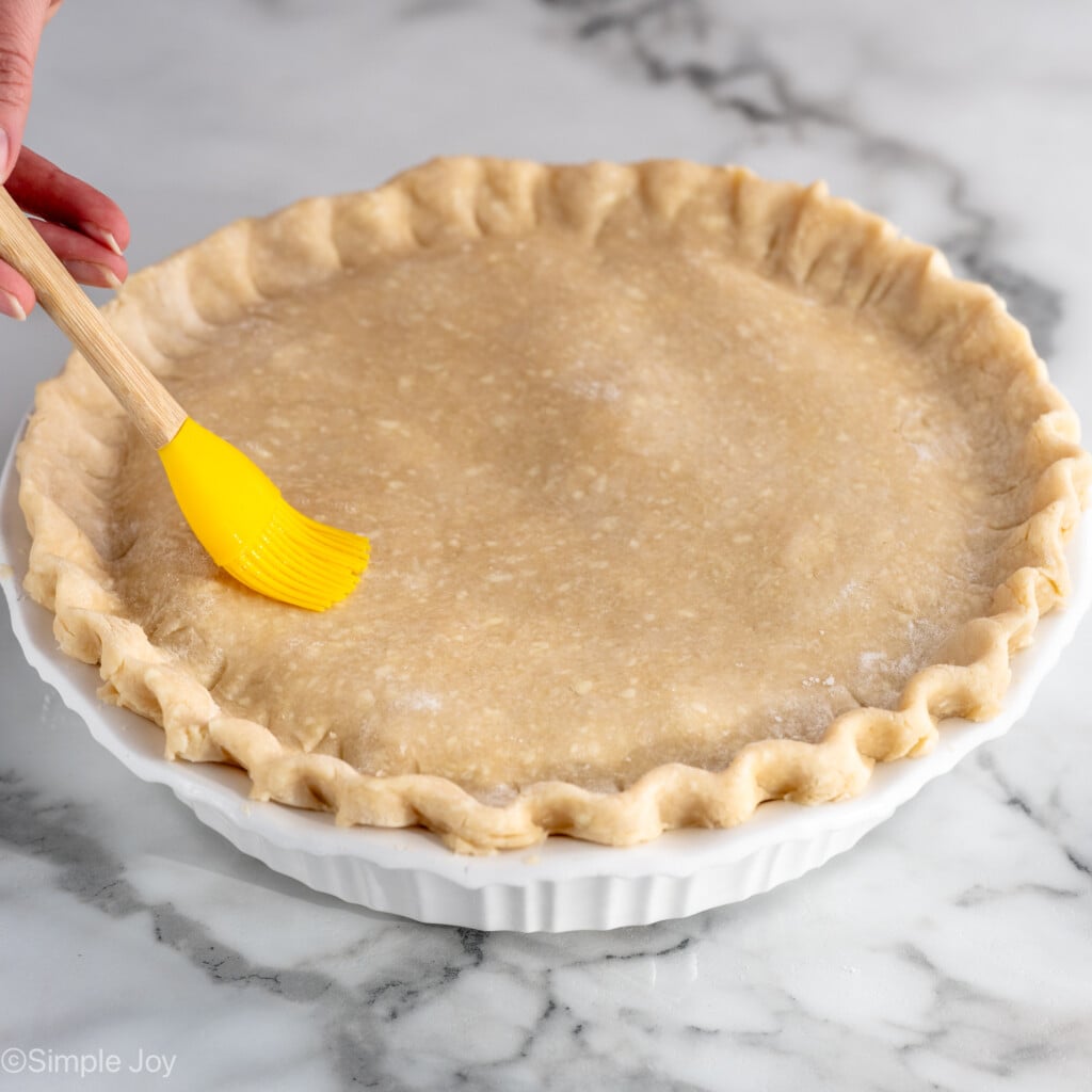 Person's hand brushing top of Chicken Pot Pie recipe before baking