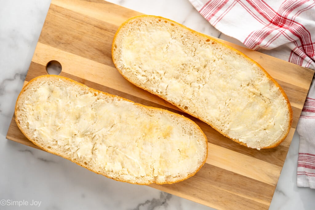 Overhead of french bread cut in half and topped with butter on a wooden cutting board to make french bread pizza - 5