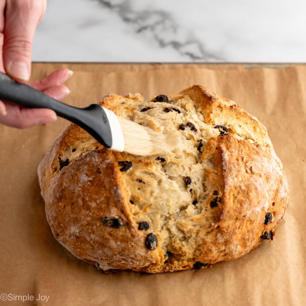 Person's hand brushing melted butter on top of loaf of Irish Soda Bread