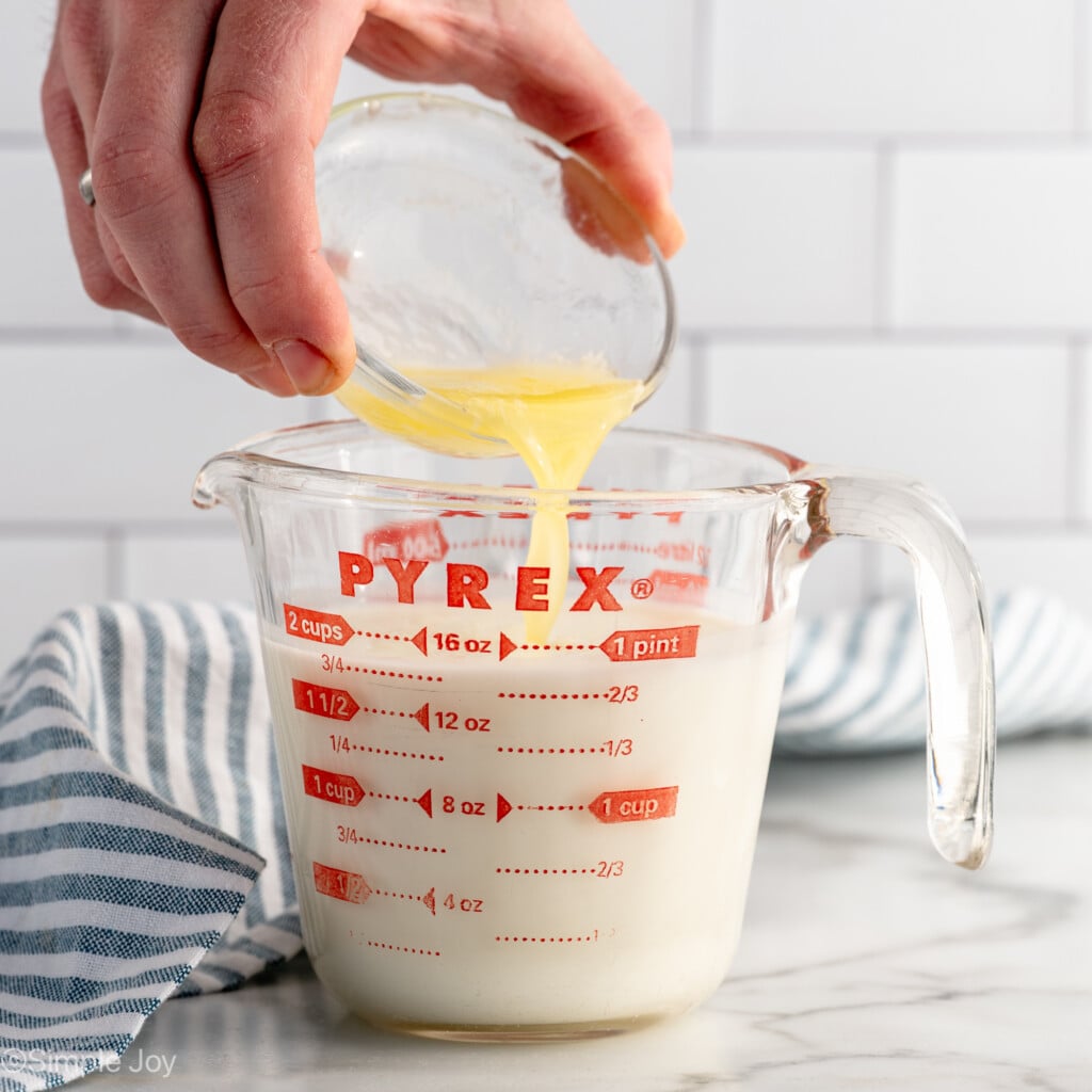 Side view of person's hand pouring lemon juice into glass measuring cup of milk to make buttermilk for Irish Soda Bread recipe