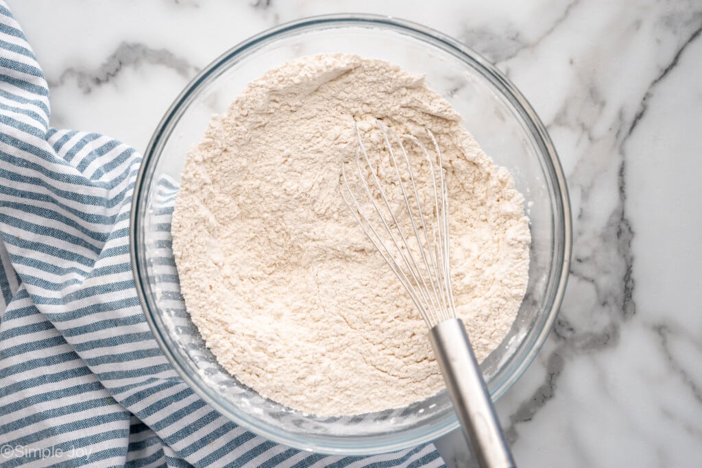 Overhead view of a mixing bowl of dry ingredients and whisk for Irish Soda Bread recipe