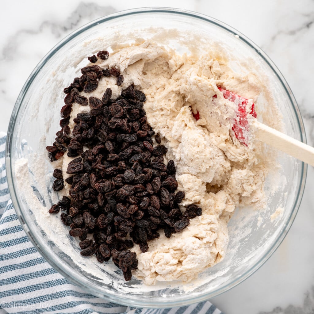 Overhead view of a mixing bowl of ingredients and raisins with spatula for Irish Soda Bread recipe
