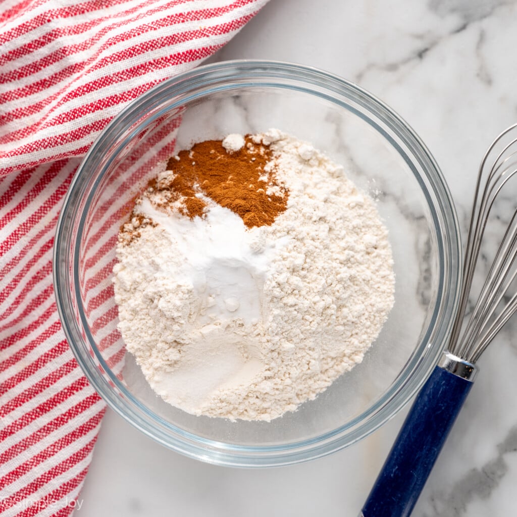 Overhead view of mixing bowl of dry ingredients for Oatmeal Raisin Cookies recipe with whisk beside