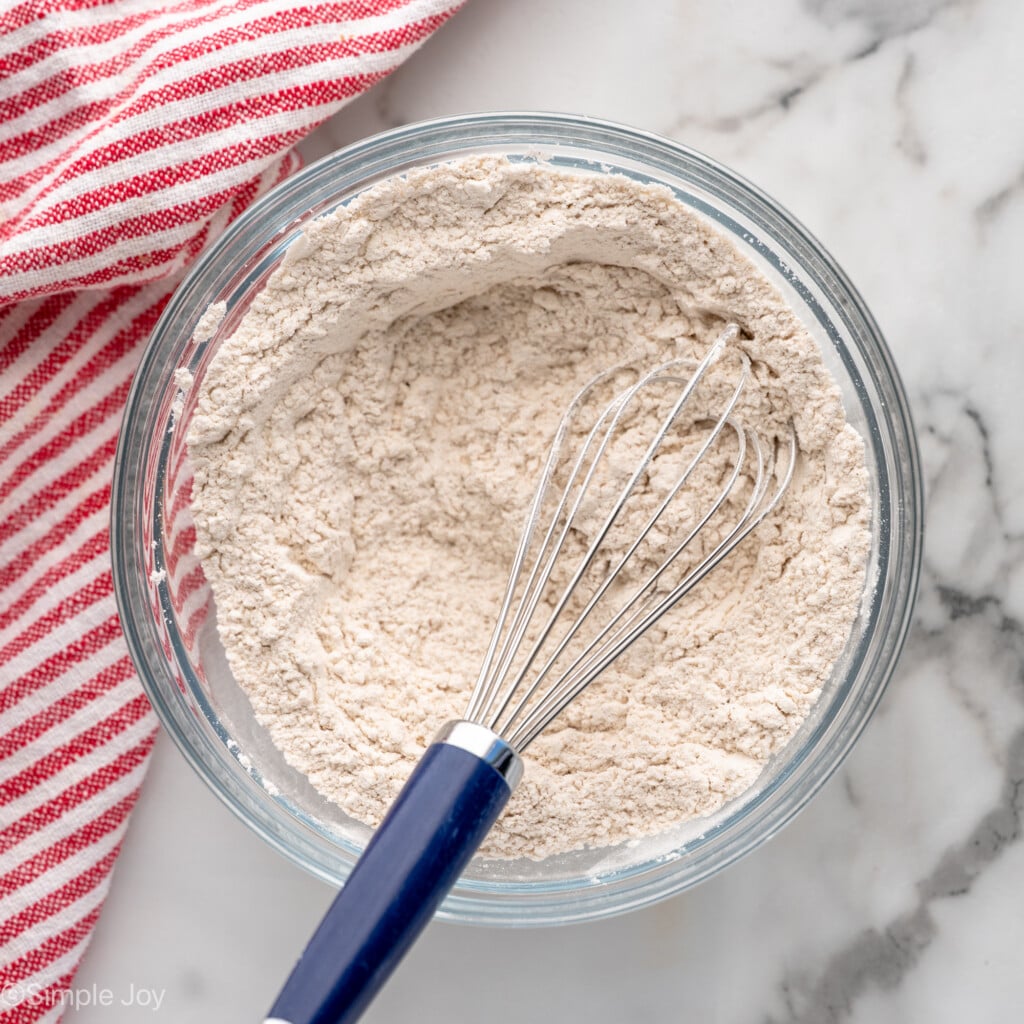 Overhead view of mixing bowl of dry ingredients and whisk after stirring for Oatmeal Raisin Cookies recipe