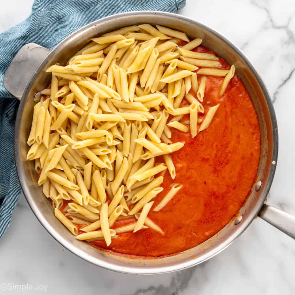 cooked penne added to a skillet with tomato sauce