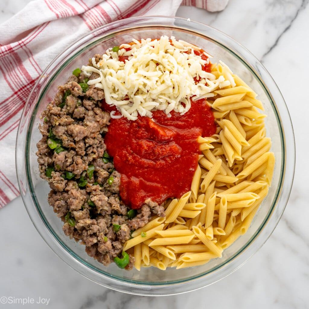 overhead of bowl of sausage, cheese, pasta sauce, and cooked pasta