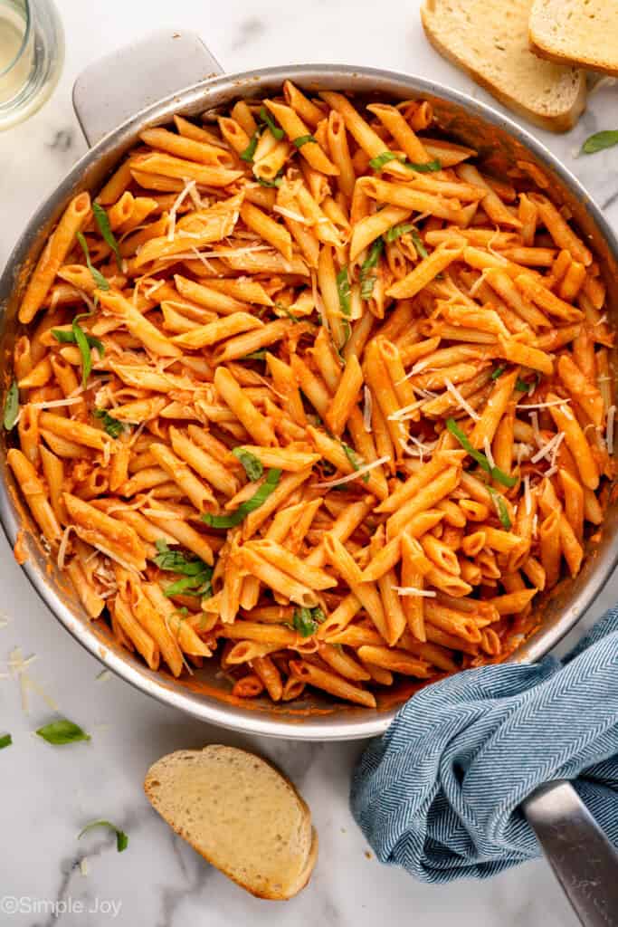 overhead of a skillet of penne alla vodka garnished with parmesan and sliced basil