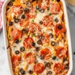 Overhead view of baking dish of Pizza Casserole garnished with shredded cheese, pepperoni, and black olives. Toast beside.