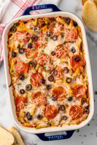 Overhead view of baking dish of Pizza Casserole garnished with shredded cheese, pepperoni, and black olives. Toast beside.