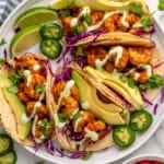 Overhead view of plate of Shrimp Tacos with avocado, limes, jalapenos, sauce, and cabbage. Pico de gallo beside