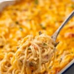 Pinterest graphic for Chicken Spaghetti. Says "the best Chicken Spaghetti simplejoy.com" Image shows serving spoon holding scoop of Chicken Spaghetti out of a baking dish of Chicken Spaghetti