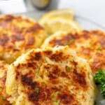 Pinterest graphic for Crab Cakes. Says "the best crab cakes recipe simplejoy.com" Image shows close up of crab cakes on a plate with lemon slices and fresh parsley.