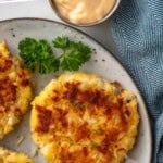 Pinterest graphic for crab cakes. Says "The Best Crab Cakes Recipe simplejoy.com" Image shows overhead of plate of crab cakes with fresh parsley and lemon slices. Cup of sauce sitting beside.
