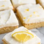 Pinterest graphic for Lemon Sugar Cookie Bars recipe. Text says, "the best lemon cookie bars simplejoy.com." Image shows sliced Lemon Sugar Cookie Bars with lemon wedges, bite taken out of one bar.